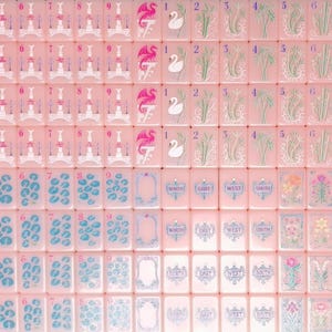 May include: A collection of rectangular mahjong tiles in a soft pink hue. The tiles feature various printed illustrations including numbered sets, swan motifs, floral patterns, directional markers labeled North, East, West, South, and Joker tiles.