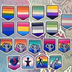 May include: A collection of colorful, shield-shaped stickers featuring various pride flags, including rainbow, bisexual, transgender, and others. Each sticker has a white border and a unique design, representing different identities and communities.