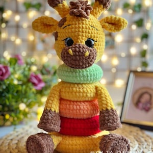 Peut inclure: Un jouet en crochet en forme de girafe avec une fourrure brune, un corps jaune et des anneaux verts, orange et rouges autour de son corps. La girafe a une expression amicale et de grands yeux bruns.