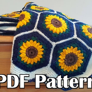 Puede incluir: Una manta de crochet con un patrón de girasol en tonos de amarillo, verde, azul y blanco. La manta está doblada y drapeada sobre una superficie de madera. El texto "PDF Pattern" es visible en la parte inferior de la imagen.