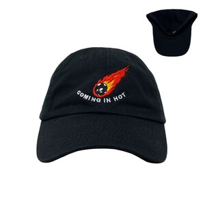 May include: A black baseball cap with an embroidered design of a soccer ball on fire with the text "COMING IN HOT".