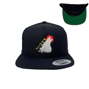 May include: A black and green snap back hat with a white wolf howling at a red sun with Japanese characters in yellow. The hat has a black brim and a green underside.