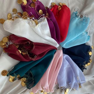 Puede incluir: Una colección de coloridas y transparentes bufandas dispuestas en forma circular. Cada bufanda es de un color diferente, incluyendo blanco, morado, rojo y azul. Monedas doradas están unidas a los bordes de cada bufanda.