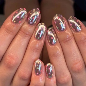 May include: Oval-shaped fingernails featuring a reflective, metallic silver chrome base coat. Each nail is decorated with small, evenly spaced polka dots in pastel shades of pink, yellow, green, and purple, creating a glossy, multi-colored finish.