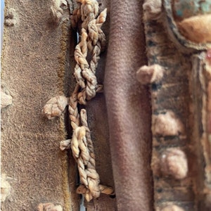 Puede incluir: Primer plano de una bolsa de cuero marr&oacute;n con una correa de cuero trenzada. La bolsa est&aacute; decorada con peque&ntilde;os trozos de cuero y una piedra turquesa.