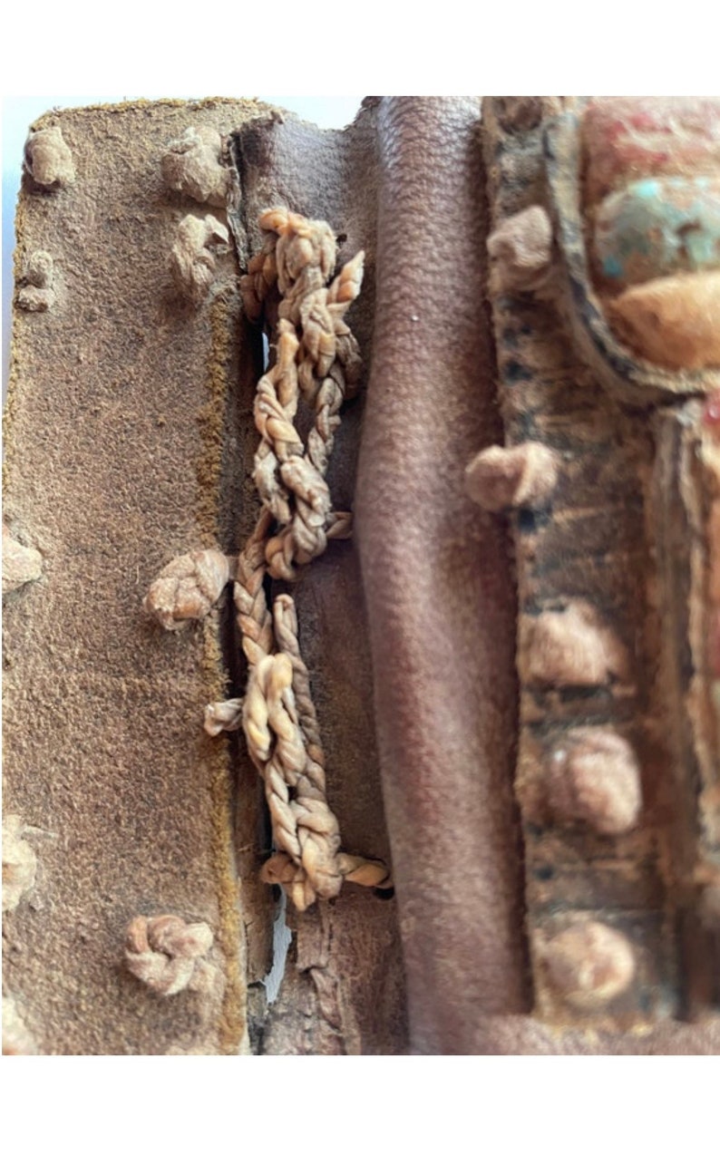 Puede incluir: Primer plano de una bolsa de cuero marr&oacute;n con una correa de cuero trenzada. La bolsa est&aacute; decorada con peque&ntilde;os trozos de cuero y una piedra turquesa.