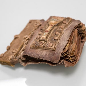 Puede incluir: Un peque&ntilde;o libro encuadernado en cuero marr&oacute;n con un cierre de metal y detalles decorativos. El libro est&aacute; cerrado y parece muy antiguo.