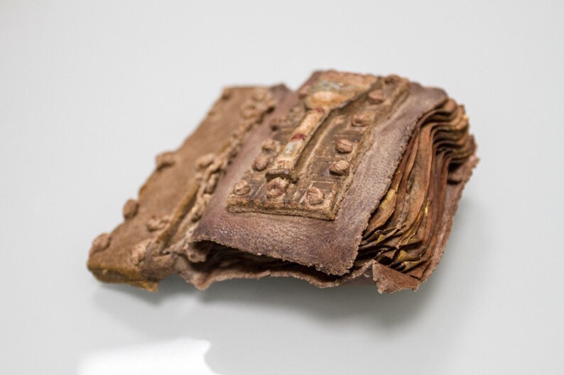 Puede incluir: Un peque&ntilde;o libro encuadernado en cuero marr&oacute;n con un cierre de metal y detalles decorativos. El libro est&aacute; cerrado y parece muy antiguo.