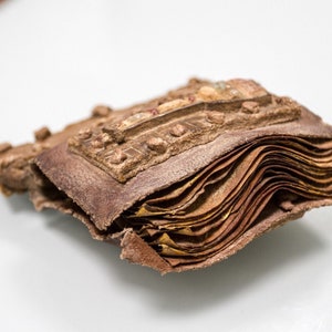 Puede incluir: Un primer plano de un libro antiguo encuadernado en cuero con una cubierta marr&oacute;n desgastada y p&aacute;ginas. El libro est&aacute; cerrado y las p&aacute;ginas son visibles a lo largo del borde.