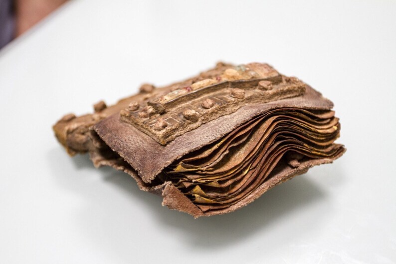 Puede incluir: Un primer plano de un libro antiguo encuadernado en cuero con una cubierta marr&oacute;n desgastada y p&aacute;ginas. El libro est&aacute; cerrado y las p&aacute;ginas son visibles a lo largo del borde.