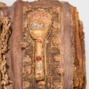 Puede incluir: Primer plano de un libro encuadernado en cuero con un cierre decorativo. El cierre es de metal y tiene un dise&ntilde;o de un objeto estilizado con pintura roja, azul y blanca.