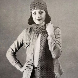 May include: A woman wearing a crocheted hat and scarf. The hat and scarf are both a light brown color and have a lacy pattern. The woman is wearing a denim jacket and jeans.