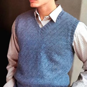 Puede incluir: Un chaleco de punto azul con un patrón diagonal, usado sobre una camisa blanca abotonada con finas rayas. El chaleco tiene cuello en V y está hecho de un hilo suave y texturizado.