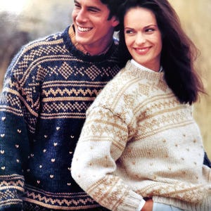 May include: A couple wearing matching patterned sweaters. The man's sweater is navy blue with a tan and white geometric design. The woman's sweater is cream with a tan and white geometric design.