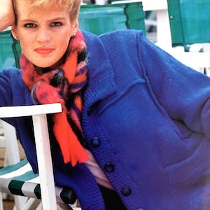 May include: A woman wearing a bright blue knitted cardigan with a red, pink, and black scarf. The cardigan has a button closure and a collar.