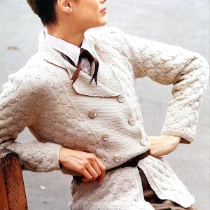 Puede incluir: Un cárdigan de punto color crema con cierre de doble botonadura y un cuello grande. El cárdigan tiene un patrón delicado y está ceñido a la cintura.