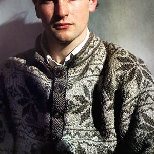 May include: A man wearing a gray and black patterned sweater with a button-up collar. The sweater has a traditional Scandinavian design.