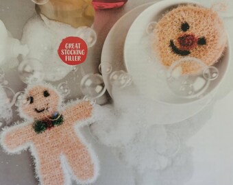 Puede incluir: Dos paños de cocina de punto con forma de hombre de jengibre. Uno es una cara redonda con una nariz roja y el otro es un hombre de jengibre de cuerpo entero con una corbata de lazo verde. Los paños de cocina están en un fondo blanco espumoso. El texto "Great Stocking Filler" está en un círculo rojo.