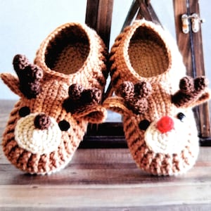 May include: A pair of brown crocheted reindeer slippers. The slippers have a red nose, black eyes, and brown antlers.