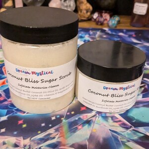 May include: Two glass jars of coconut bliss sugar scrub with black lids. The labels are white with black text that reads "Dream Mystical Coconut Bliss Sugar Scrub Exfoliate-Moisturize-Cleanse".