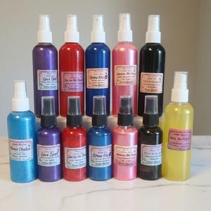 Puede incluir: Una variedad de botellas de spray coloridas, cada una con una etiqueta blanca y una tapa del mismo color. Las botellas están dispuestas en grupo, con varios tamaños y colores, incluyendo azul, morado, rojo, rosa y amarillo. Las etiquetas tienen texto.