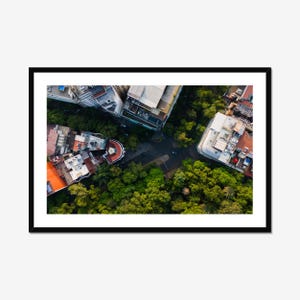Può includere: Una vista aerea di un incrocio cittadino con edifici e alberi. Gli edifici sono principalmente in mattoni e cemento, alcuni con tetti in tegole rosse. Gli alberi sono verdi e rigogliosi, e l'incrocio è pavimentato con asfalto.