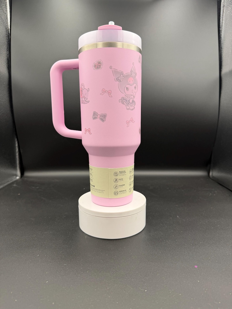 Puede incluir: Taza de viaje aislada rosa con asa, con un dise&ntilde;o de personaje de dibujos animados y detalles de lazo. La taza tiene una tapa blanca y una banda plateada. Est&aacute; sobre una base circular blanca.