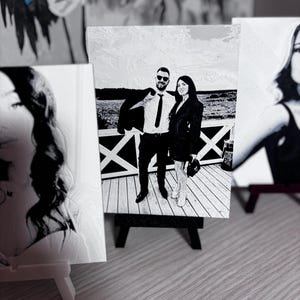 Può includere: Foto in bianco e nero di una coppia in piedi su un ponte di legno. L'uomo indossa un abito e una cravatta, e la donna indossa un vestito. La foto è stampata su tela e montata su un piccolo cavalletto.