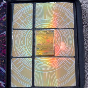 May include: A black zippered trading card binder featuring a gold holographic insert with a circular geometric pattern. A single gold-colored Mega Greninja GX trading card with 350 HP is displayed in the center pocket of the nine-pocket page.