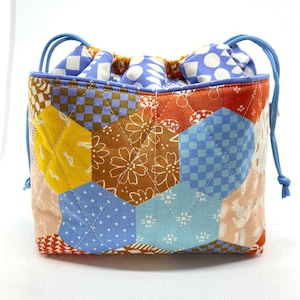 May include: A blue and brown patchwork drawstring bag with a hexagonal pattern. The bag is made of quilted fabric and has a drawstring closure.