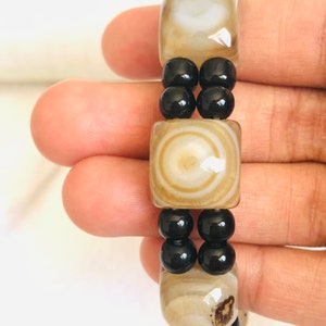 May include: A bracelet made of brown and white agate beads with black beads in between.