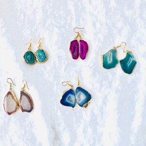 May include: Assortment of six pairs of agate earrings. Each pair features a different color and pattern of agate, including pink, blue, and green. The earrings are all gold-plated and have a simple, elegant design.
