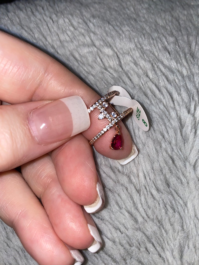 May include: A gold ring with a red gemstone and clear stones. The ring is size 8.