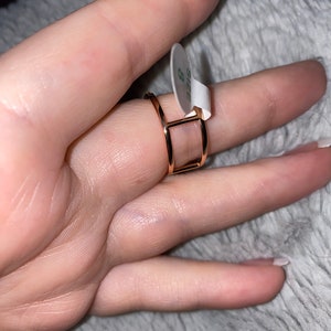 May include: A gold-toned ring with a square design. The ring is on a finger and has a size 8 tag attached.