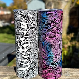 May include: Two stainless steel tumblers with a black and white mandala design and a pink and blue mandala design. The tumbler on the left has the name "Victoria" written on it.