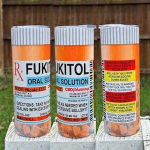 May include: Three orange and white pill bottle-shaped tumblers with the text "FUKITOL ORAL SOLUTION" and "CBD Pharmacy" on them. The tumblers are filled with orange pills.