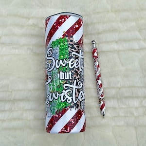 May include: A stainless steel tumbler and pen set. The tumbler features a red and white striped design with glitter accents and the words "Sweet but Twisted." The pen has a matching design.