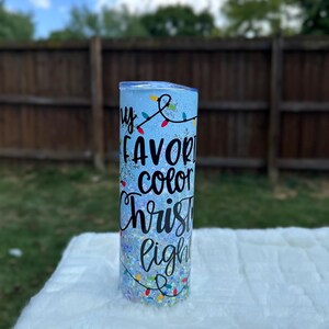 May include: A blue tumbler with glitter and a white design that says "My favorite color Christmas lights".