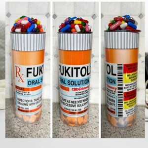 May include: A tall orange and white pill bottle tumbler with a lid. The bottle is labeled "RFUK UKITOL ORAL SOLUTION CBD Pharmacy". The lid is filled with colorful pills.