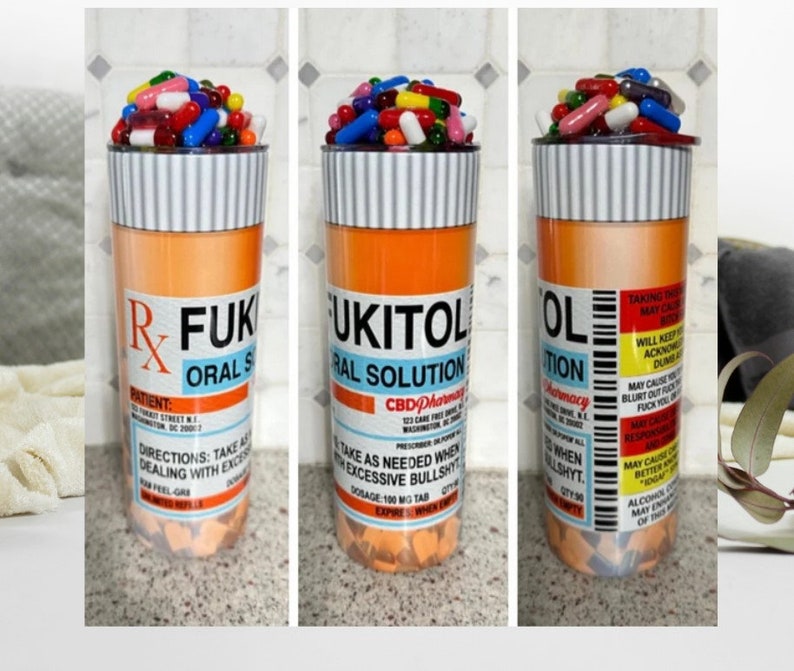May include: A tall orange and white pill bottle tumbler with a lid. The bottle is labeled "RFUK UKITOL ORAL SOLUTION CBD Pharmacy". The lid is filled with colorful pills.