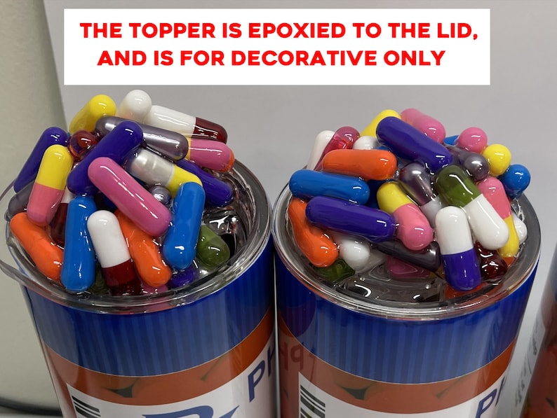 May include: Two clear glass cups filled with colorful capsules. The cups are blue and red with white text. The text on the cups reads "THE TOPPER IS EPOXIED TO THE LID, AND IS FOR DECORATIVE ONLY".
