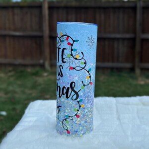 May include: A blue and white tumbler with a glitter finish. The tumbler has a design of colorful Christmas lights and the text "It is Christmas".