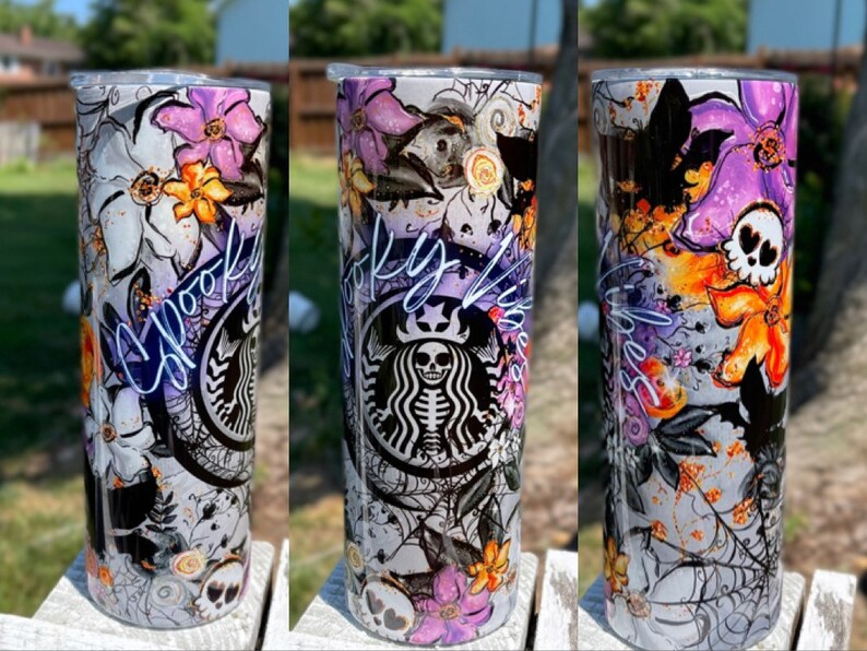 May include: A tall, stainless steel tumbler with a Halloween-themed design. The design includes purple and orange flowers, spiderwebs, bats, and a skull. The Starbucks logo is visible, with a skeleton in place of the usual figure. The word "Spooky" is written in cursive.