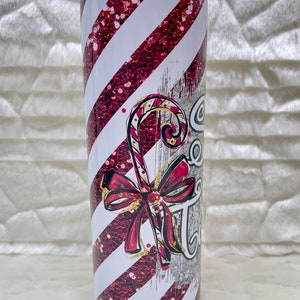 May include: A stainless steel tumbler with a festive candy cane design. The tumbler features diagonal white and red glitter stripes, a candy cane graphic, and the text "Sweet Treats". A red bow accents the candy cane.