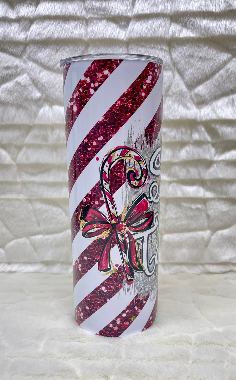 May include: A stainless steel tumbler with a festive candy cane design. The tumbler features diagonal white and red glitter stripes, a candy cane graphic, and the text "Sweet Treats". A red bow accents the candy cane.