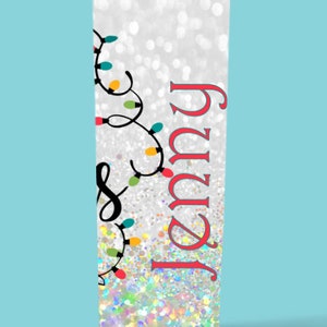 May include: A white tumbler with a silver glitter finish and a design of colorful Christmas lights and the name "Jenny" in red.