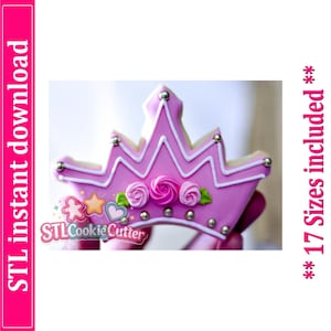 May include: A crown-shaped cookie decorated with pink icing, white piping, three pink icing roses with green leaves, and silver edible beads. The text reads STL instant download and 17 Sizes included. The design features a five-point crown shape.