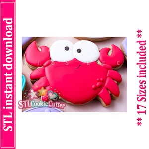 May include: A crab-shaped cookie decorated with bright red icing for the body and claws, and large white icing eyes with black pupils. The text STL instant download and 17 Sizes included are visible on the sides of the image along with a logo.