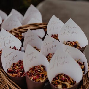 A basket filled with white paper cones containing red and yellow flower petals, with each cone labeled with the names "Schwab and Fustar".