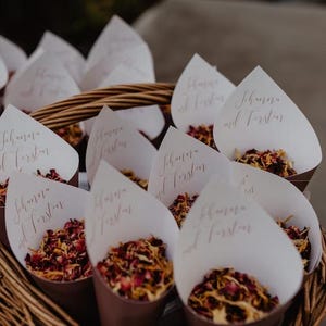 A basket filled with white paper cones containing red and yellow flower petals, with each cone labeled with the names "Schwab and Fustar".